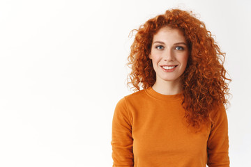 Happy cute redhead woman with curly hair smiling sincere and carefree, standing white background...