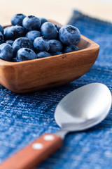 Blueberries in a wood bowl on top of blue and white napkin with a spoon