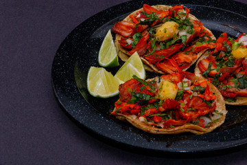 Tacos al pastor de carne de puerco con cilantro, cebolla y piña montados sobre un plato negro