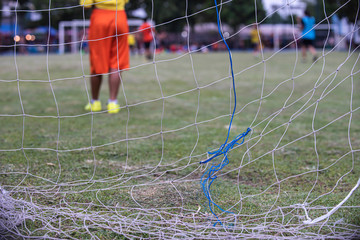 Boy elementary local soccer team practicing tactics and drilling on a green pitch with their coach after a school day in the evening. Selective focus on the field and net. A local sport youth centre.