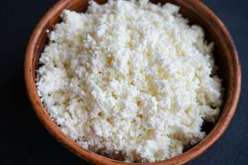 Cottage cheese in a brown bowl on a dark background. Dietary food with calcium.