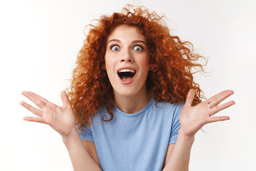 Close-up shot emotive, attractive redhead curly-haired woman, raising hands up surprised and overwhelmed, shouting impressed, stare camera astonished, dancing in rejoice, white background