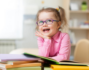 Smart kid girl in eye glasses reading books in her room