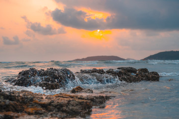 Sea waves crashing against rocks At sunrise, the color is orange.