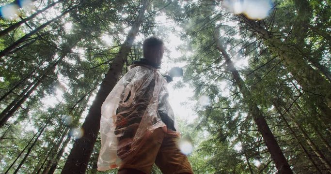 Low angle of young cheerful man hiker taking selfie pictures on camera against green tall trees rainy forest background.