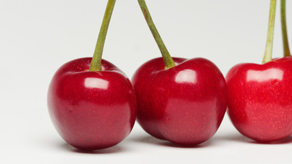 Three red ripe cherry fruits isolated on white background with shadows.