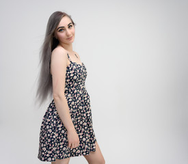 Studio portrait of a knee-length of a pretty student girl with long beautiful hair in a beautiful color dress on a white background. He stands straight, smiles, shows with his hands.