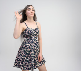 Fototapeta premium Studio portrait of a knee-length of a pretty student girl with long beautiful hair in a beautiful color dress on a white background. He stands straight, smiles, shows with his hands.