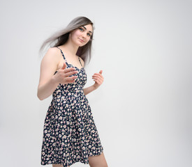 Studio portrait of a knee-length of a pretty student girl with long beautiful hair in a beautiful color dress on a white background. He stands straight, smiles, shows with his hands.