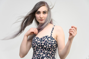 Studio portrait of a pretty student girl with long beautiful hair in a beautiful color dress on a white background. He stands straight, smiles, shows with his hands.