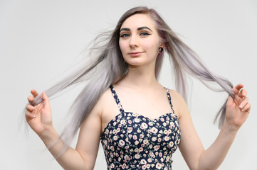 Fototapeta premium Studio portrait of a pretty student girl with long beautiful hair in a beautiful color dress on a white background. He stands straight, smiles, shows with his hands.