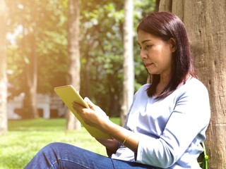 Obraz premium Portrait woman using digital tablet while sitting in the park, smile, relaxing, beautiful garden. Selective focus with noise and blurry bokeh background.