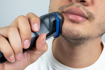 Close up of a young man shaving with electric razor.