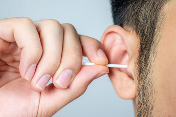 A young man asia using a stick of cotton swab for ears cleaning. Daily hygiene. Light gray...
