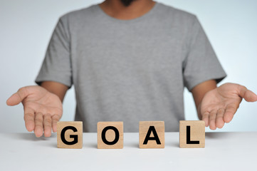 Business success for goal concept. Wooded cube block on a person standing as a background with word goal