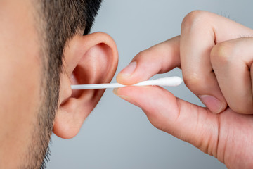 A young man asia using a stick of cotton swab for ears cleaning. Daily hygiene. Light gray background. Close up.