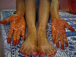 indian woman's hand and leg painted with orange henna or mehendi