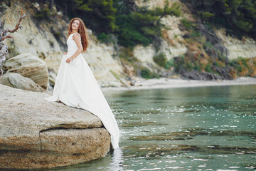 Beautiful long-haired bride in a magnificent white dress walking near water