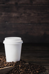 Takeaway cup of coffee with beans on brown wooden background