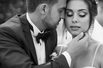 A young and beautiful bride and her husband is standing in a summer park with bouquet of flowers
