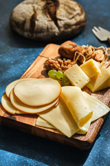 Different varieties of cheese with grapes and walnuts on a wooden board.