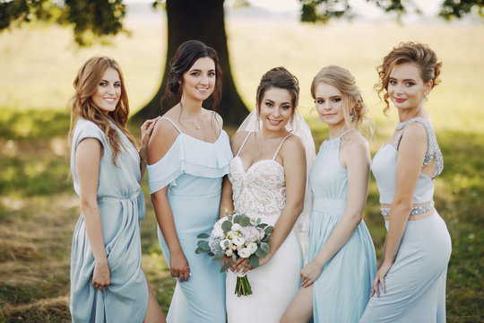 elegant and stylish bride along with her four girlfriends in blue dresses standing in a park