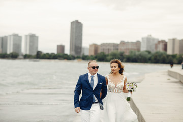 Beautiful bride in a long white dress. Handsome fiance in a blue suit. Couple near ocean