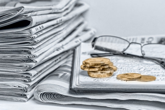 A stack of folded newspapers on the desktop in the office. Latest financial and business news in daily paper. Coins, glasses for sight.