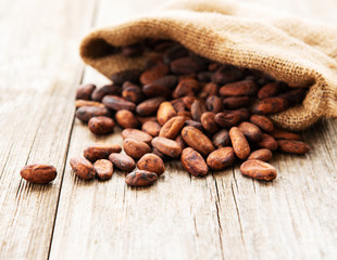 Raw cacao beans in burlap bag on a wooden table