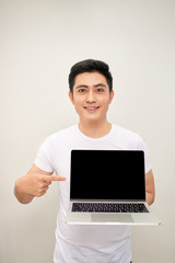 Smiling young asian man dressed in shirt showing blank screen laptop computer over white background