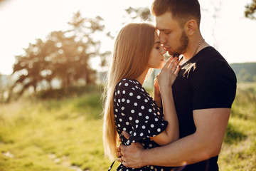 Fototapeta premium Cute couple in a park. Lady in a black dress. Guy in a black t-shirt.
