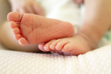 Tiny delicate feet of newborn baby on a bed.