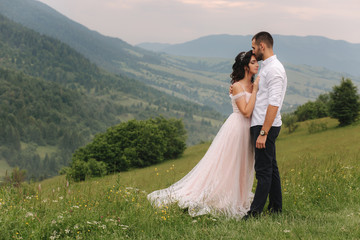 Beautiful young wedding couple standing on the green slope, hill. Groom and bride in Carpathian mountains