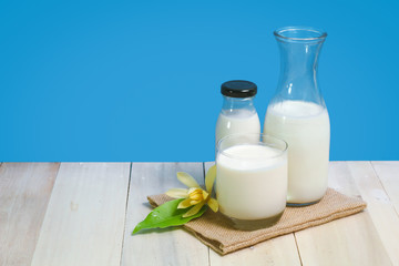 A bottle of rustic milk and glass of milk on a wooden table on a blue background