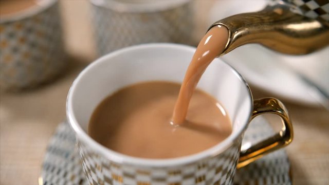 Tea being poured into beautiful cup from a teapot . 
