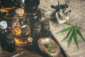 CBD oil bottles and green plant of cannabis on a wooden background. Herbal medicine.