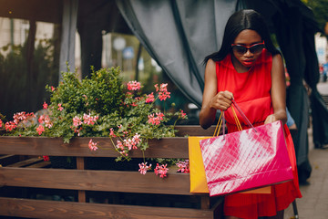 Black girl in a summer city. Woman with a shoping bags. Lady in a red ress