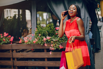 Black girl in a summer city. Woman with a shoping bags. Lady in a red ress