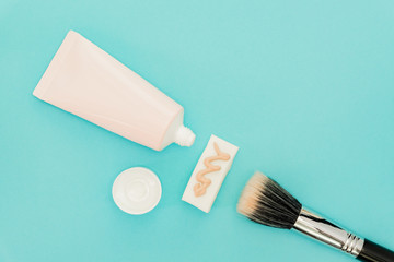 Liquid fluid foundation in tube on makeup sponge and brush makeup on blue background.