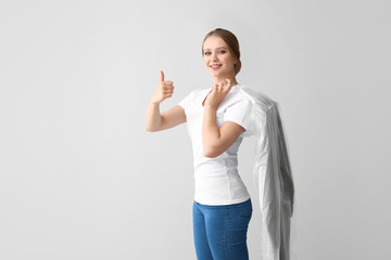Woman with clothes after dry-cleaning showing thumb-up on light background
