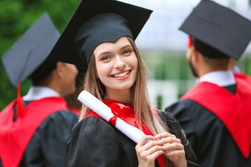 Female student in bachelor robe and with diploma outdoors