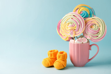 Baby knitted shoes for newborns and rainbow sweetness on blue background, Minimal baby shower, newborn party background, copy space