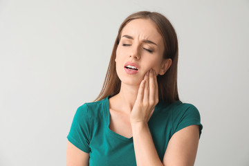 Young woman suffering from toothache against light background