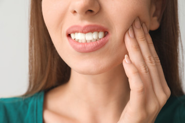 Young woman suffering from toothache against light background, closeup