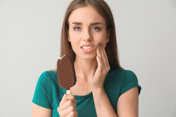 Young woman with sensitive teeth and cold ice-cream on light background