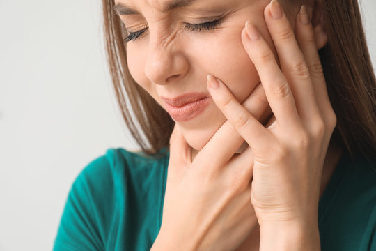 Young woman suffering from toothache against light background, closeup