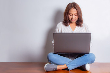 Fototapeta premium Happy smiling asian woman working on laptop computer while sitting on the floor with legs crossed isolated on white background