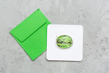 Minimal composition with a paper greeting card with watermelon and green envelope on a gray concrete background. Mockup, copy space, overhead. Flat lay. Top view.