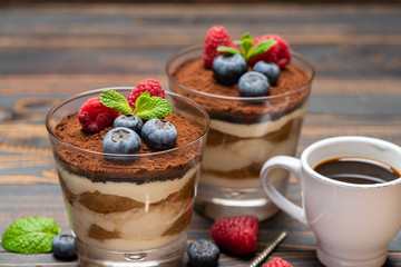 Classic tiramisu dessert with blueberries and strawberries in a glass cup and espresso coffee on wooden background