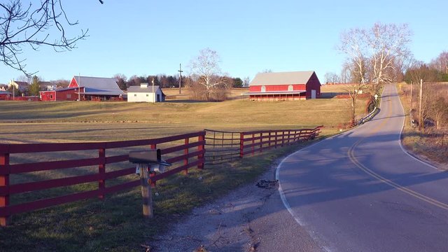 A pickup truck passes on a road near a pretty farm in this all American country rural midwest scene.